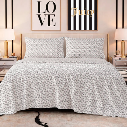 A neatly made bed features the Printed Microfiber Sheet Set in white and gray, flanked by mirrored nightstands and gold lamps. Behind the bed, two framed prints—one reading LOVE, the other Juicy—complete the luxurious look.