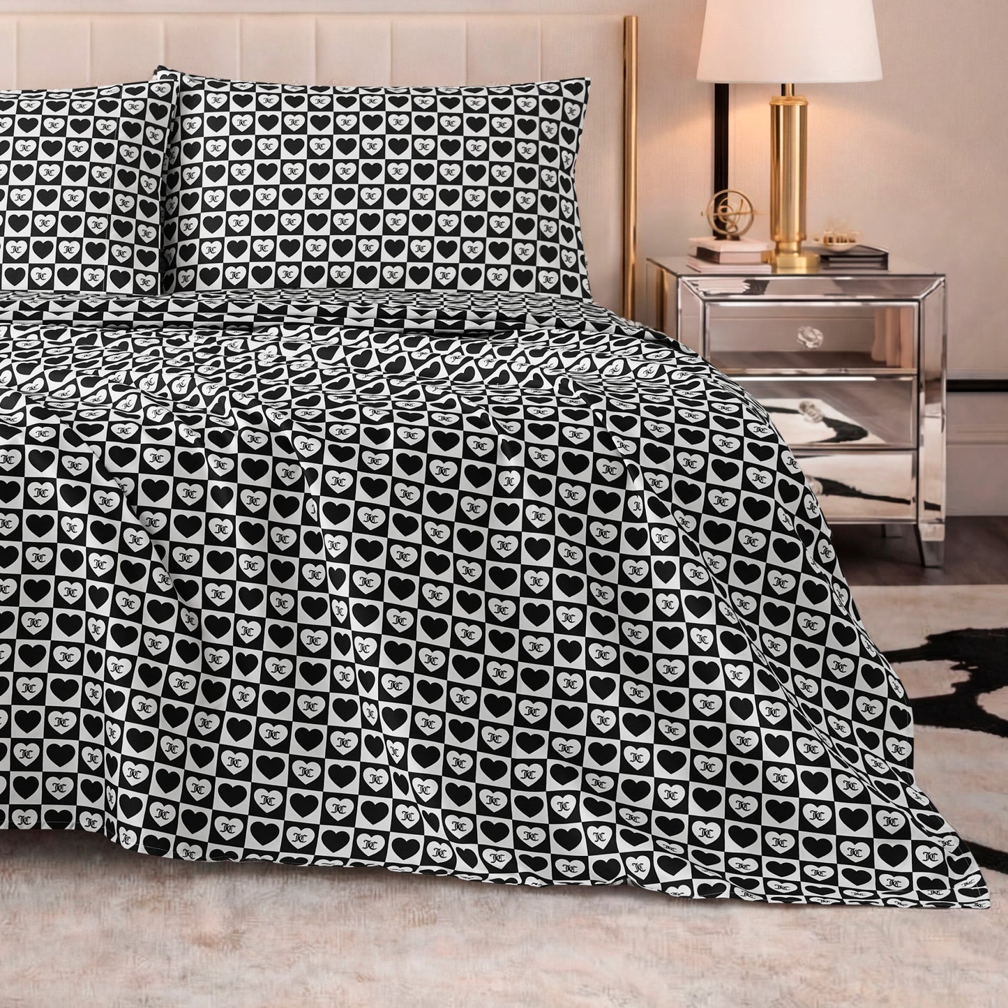 A bed with a Printed Microfiber Sheet Set in black and white heart pattern, two matching pillows, a mirrored nightstand with a lamp, and modern neutral decor.