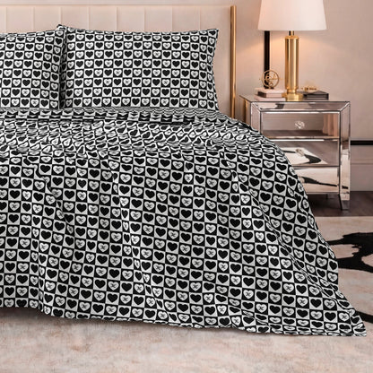 A bed with a Printed Microfiber Sheet Set in black and white heart pattern, two matching pillows, a mirrored nightstand with a lamp, and modern neutral decor.