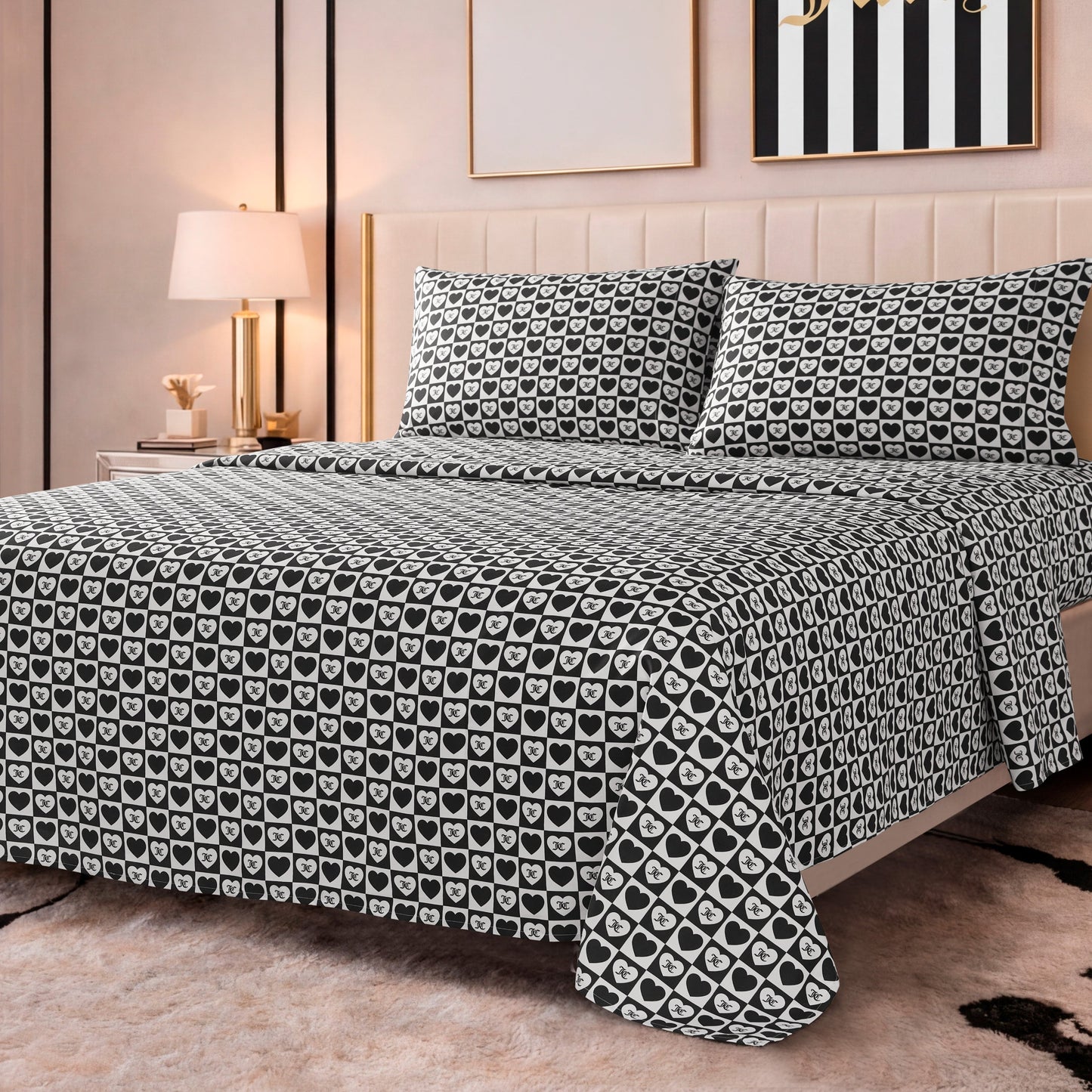 A neatly made bed features the Printed Microfiber Sheet Set in black and white with a repeating heart pattern, set in a modern bedroom with light walls, a lamp, and framed artwork above the bed.