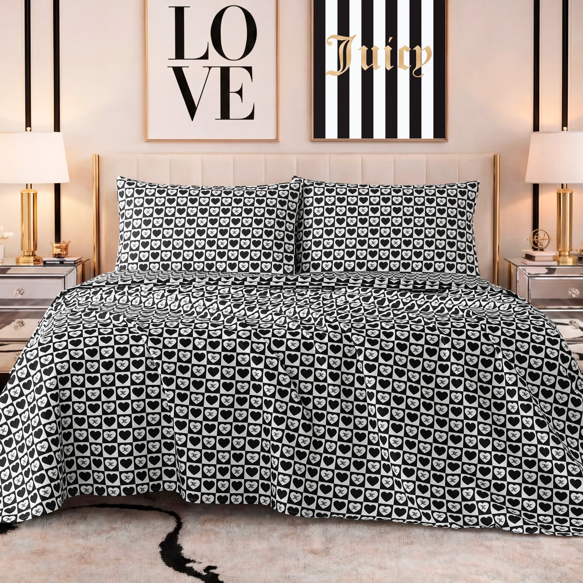 A stylish bedroom features a bed with a black and white heart-patterned comforter, matching pillows, a Printed Microfiber Sheet Set, gold lamps on mirrored nightstands, and LOVE and Juicy wall art above the headboard.