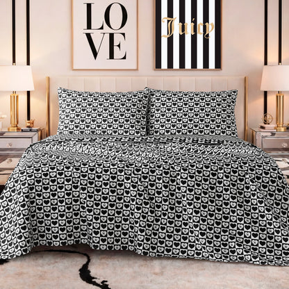 A stylish bedroom features a bed with a black and white heart-patterned comforter, matching pillows, a Printed Microfiber Sheet Set, gold lamps on mirrored nightstands, and LOVE and Juicy wall art above the headboard.