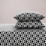 Two stacked pillows and a bed are dressed in the Printed Microfiber Sheet Set with black-and-white hearts featuring XO inside each heart, bringing stylish charm to your bedroom against a plain light-colored wall.