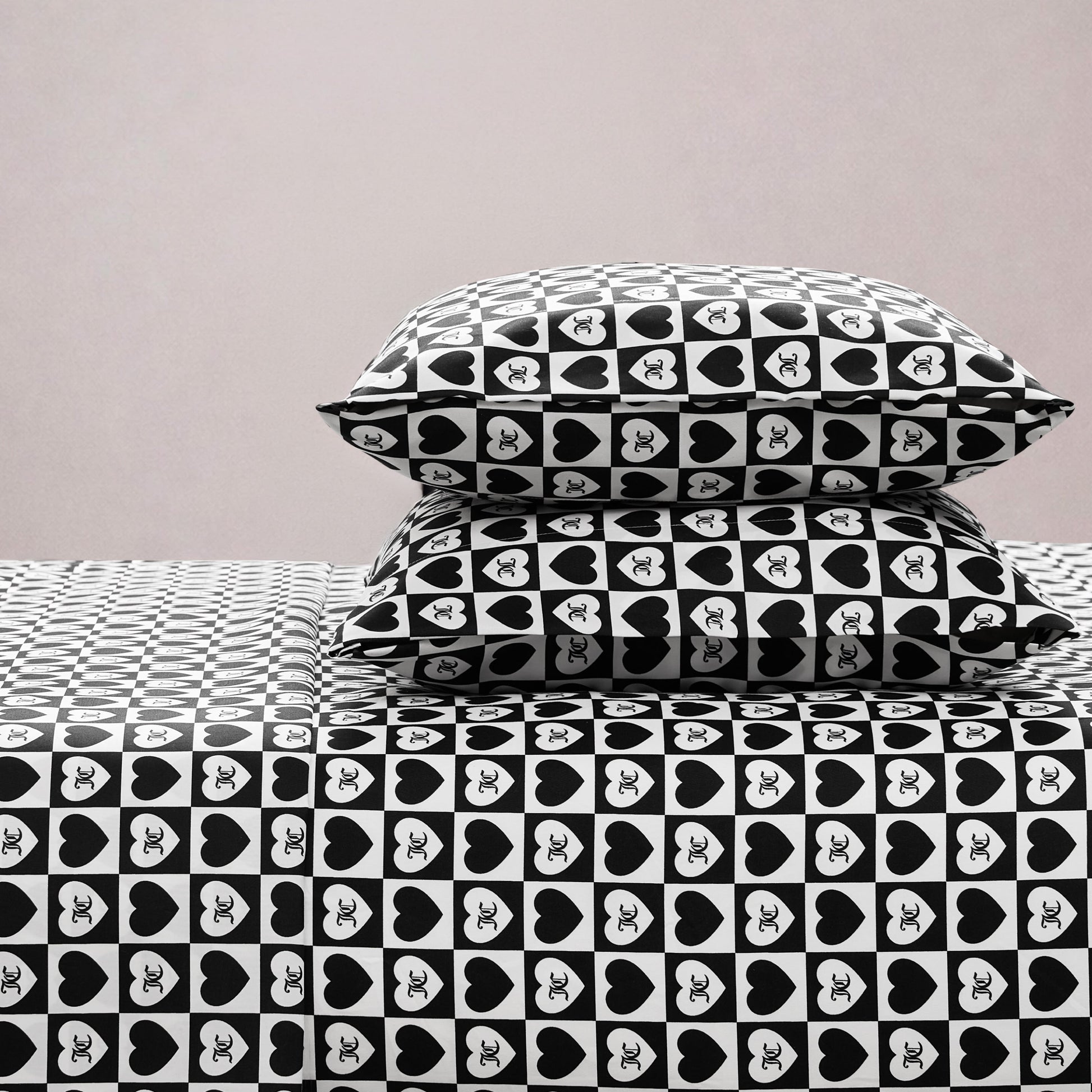 Two stacked pillows and a bed are dressed in the Printed Microfiber Sheet Set with black-and-white hearts featuring XO inside each heart, bringing stylish charm to your bedroom against a plain light-colored wall.