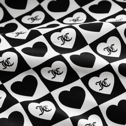 The Printed Microfiber Sheet Set features black and white checkerboard squares with alternating hearts, each displaying a stylized overlapping MC monogram. The luxury bedding surface has a subtle wavy texture.