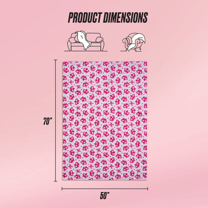 A Kids Plush Throw Blanket with a pink and white cartoon pattern is displayed on a pink background. The ultra-soft throw, shown draped over a sofa and person, measures 70 by 50 inches. Text reads Product Dimensions.