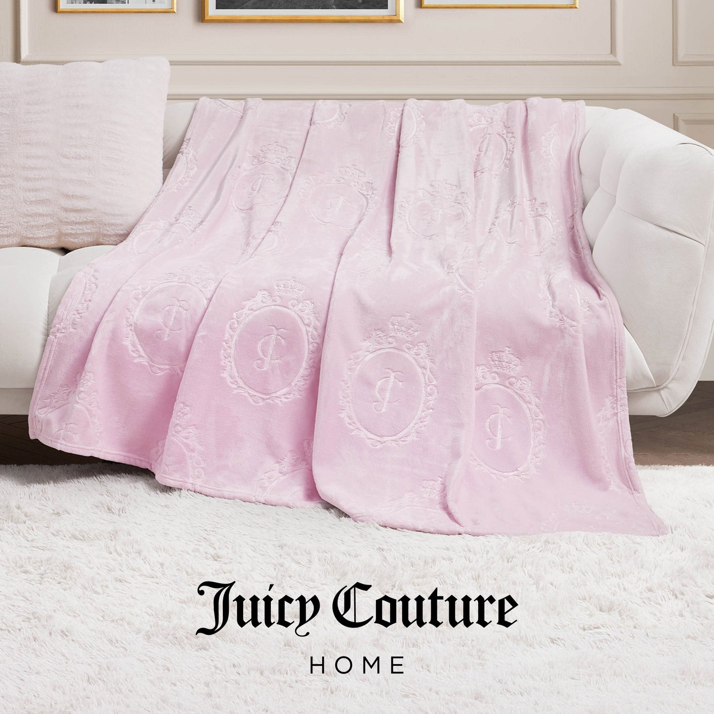 A light pink Plush Oversized Throw Blanket (60" x 90") with embossed logo patterns is draped over a white couch in a chic living room, featuring "Juicy Couture HOME" text at the bottom.