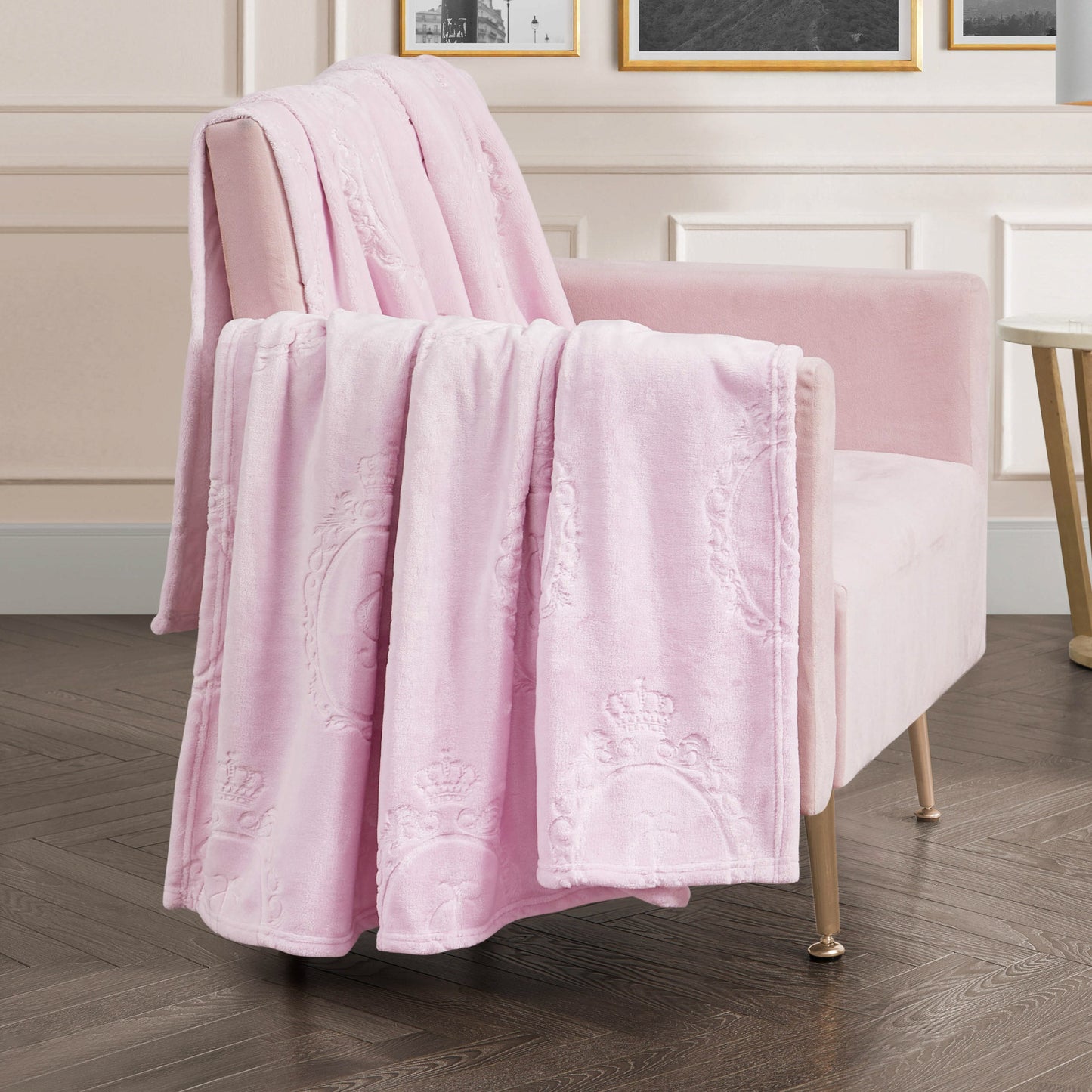 A soft pink armchair with a Plush Oversized Throw Blanket (60" x 90") draped over it sits on a dark wood floor in an elegant, light-hued room adorned with framed artwork.