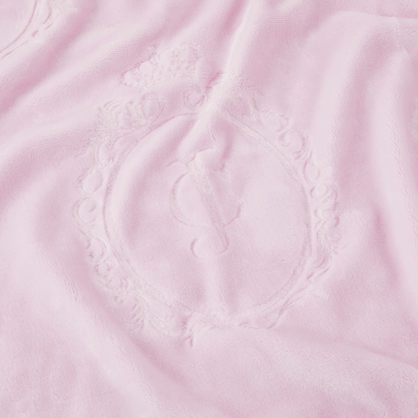 A close-up of the Plush Oversized Throw Blanket, 60" x 90", in soft light pink, featuring an embossed ornate oval frame with a script "J" in the center and a small crown above the frame.