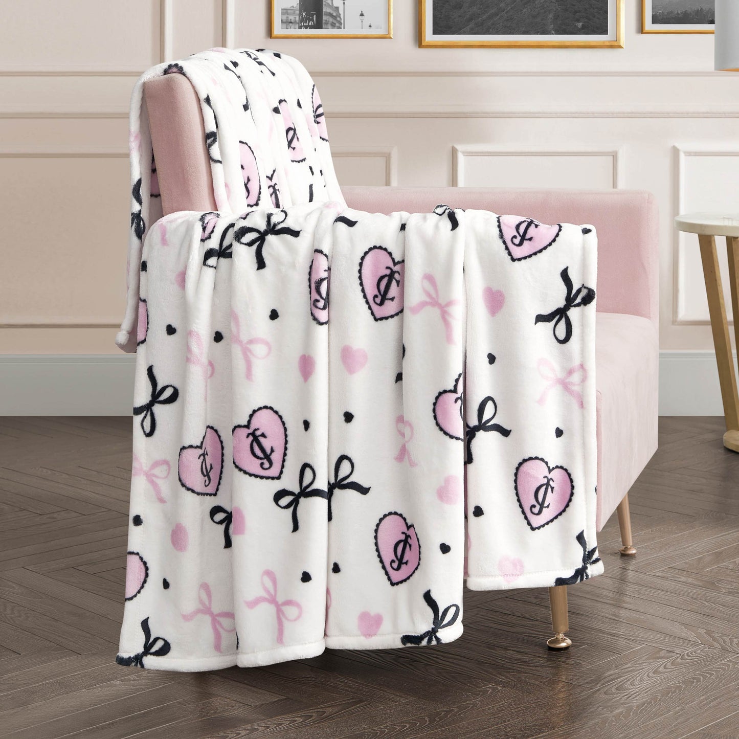 A Plush Oversized Throw Blanket in soft white with pink hearts, pink and black bows, and black polka dots is draped over a pale pink armchair, bringing cozy charm to a modern living room.