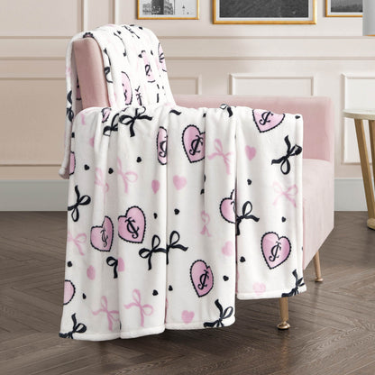 A Plush Oversized Throw Blanket in soft white with pink hearts, pink and black bows, and black polka dots is draped over a pale pink armchair, bringing cozy charm to a modern living room.