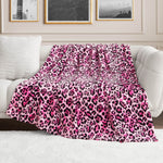 A stylish living room features a plush white sofa draped with the Plush Oversized Throw Blanket in pink and black leopard print, framed black-and-white photos on the wall, and a soft white rug on the floor.