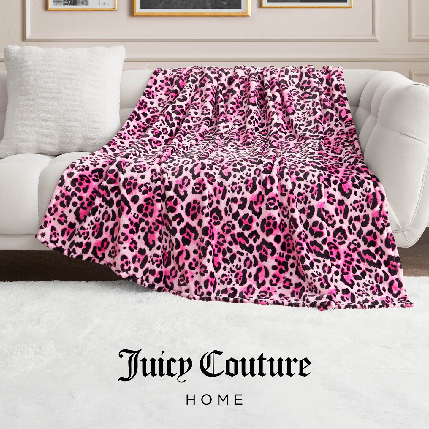 A Plush Oversized Throw Blanket with pink, black, and white leopard print is draped over a cream sofa with a white cushion. A white rug covers the floor, and Juicy Couture Home appears at the bottom.