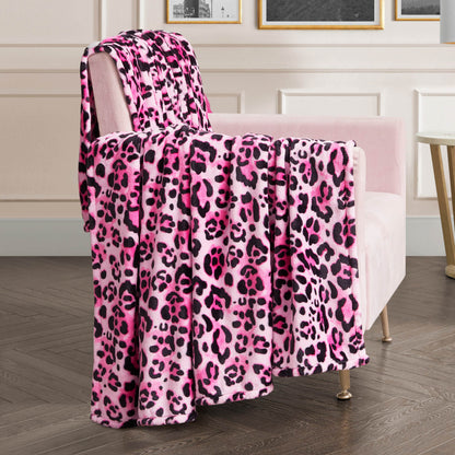 A stylish room with wood flooring and framed artwork features a plush pink chair draped with the Plush Oversized Throw Blanket in pink, black, and white leopard print over the back and seat.