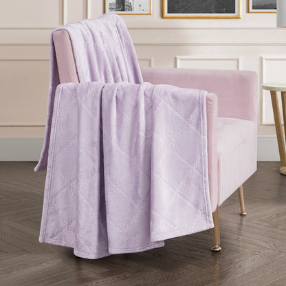 A Plush Oversized Throw Blanket, 60" x 90", in soft lavender with a diamond pattern is draped over a light pink velvet armchair in a chic living room with wood flooring and white paneled walls.