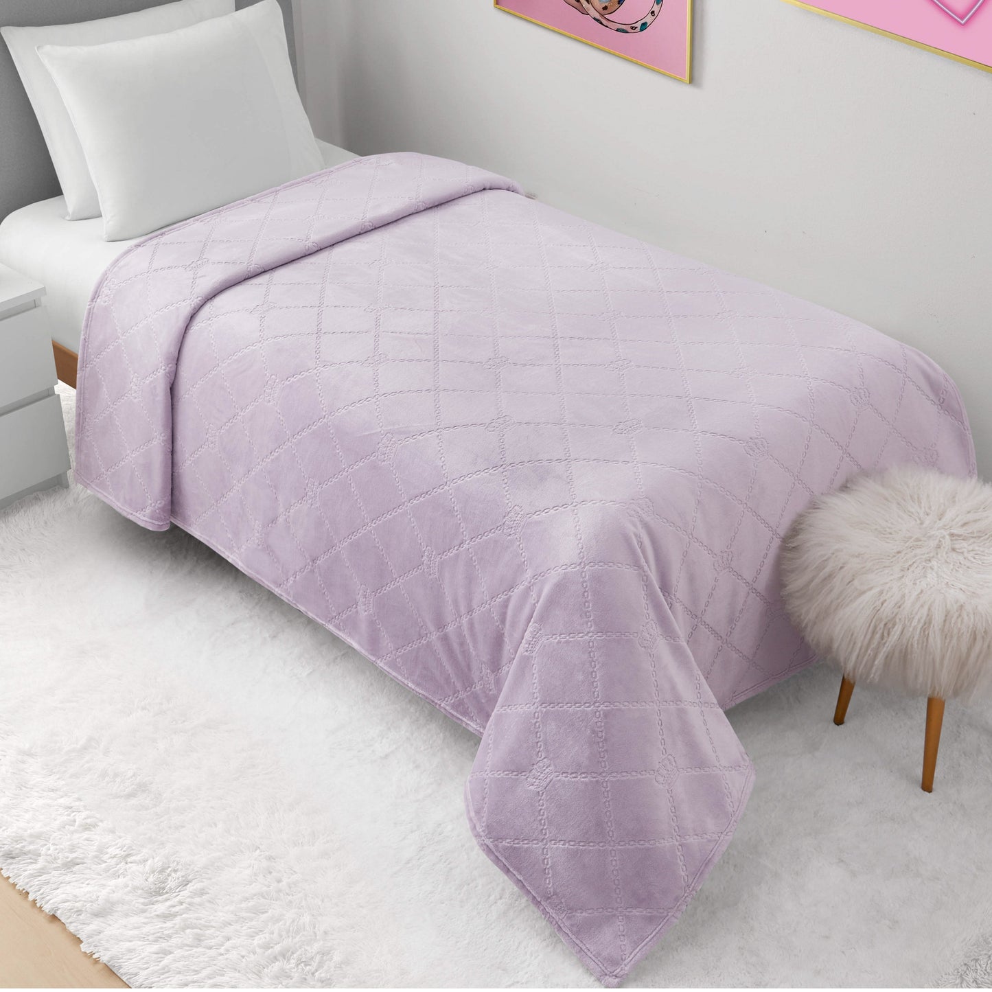 A neatly made bed with a light purple quilted blanket, Plush Oversized Throw Blanket (60" x 90"), white pillow, nightstand, round fluffy stool, and white rug in a bright modern bedroom. Pink wall art hangs above the bed.