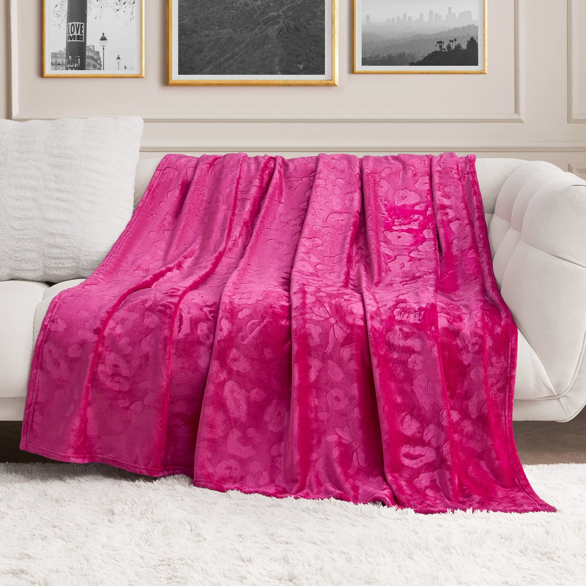 A Plush Oversized Throw Blanket, 60" x 90", in bright pink, is draped over a white sofa in a modern living room with framed black-and-white photos on the wall and a white shag rug on the floor.