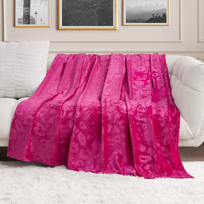 A Plush Oversized Throw Blanket, 60" x 90", in bright pink, is draped over a white sofa in a modern living room with framed black-and-white photos on the wall and a white shag rug on the floor.