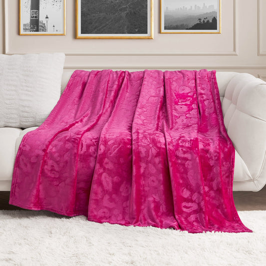 A Plush Oversized Throw Blanket, 60" x 90", in bright pink, is draped over a white sofa in a modern living room with framed black-and-white photos on the wall and a white shag rug on the floor.