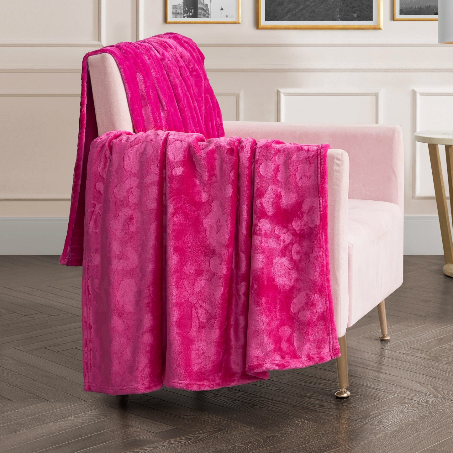 A soft pink armchair with gold legs is draped with the Plush Oversized Throw Blanket, 60" x 90", in bright pink. The chair sits on dark wood flooring in a modern room with white paneled walls and framed pictures.