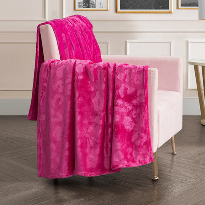 A soft pink armchair with gold legs is draped with the Plush Oversized Throw Blanket, 60" x 90", in bright pink. The chair sits on dark wood flooring in a modern room with white paneled walls and framed pictures.