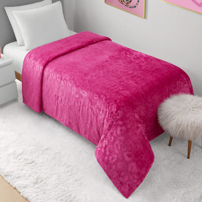 A neatly made bed with a vibrant pink Plush Oversized Throw Blanket (60" x 90") and white pillows sits by a white nightstand. A fluffy white stool rests on a soft rug, while pink art accents the light gray wall for chic style.