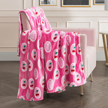 A Plush Oversized Throw Blanket with a cherry and oval pattern in pink is draped over a pale pink armchair in a modern living room with white walls and framed art—the perfect ultra-soft accent for cozying up.