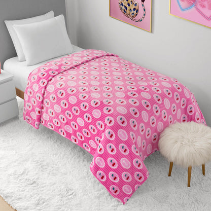 A neatly made twin bed features a Plush Oversized Throw Blanket in pink and white emoji pattern, with white bedding on a fluffy rug. Nearby are a furry stool, white nightstand, and framed wall art in this modern, bright room.