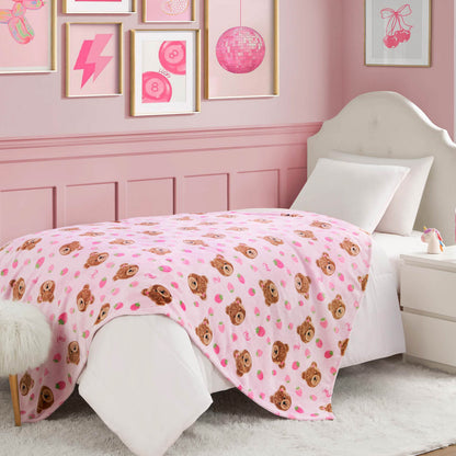 A cozy pink bedroom features a white bed topped with the Kids Plush Throw Blanket, ultra-soft and adorned with teddy bear faces. Framed pink art decorates the walls, and a nightstand sits beside the bed for extra charm.
