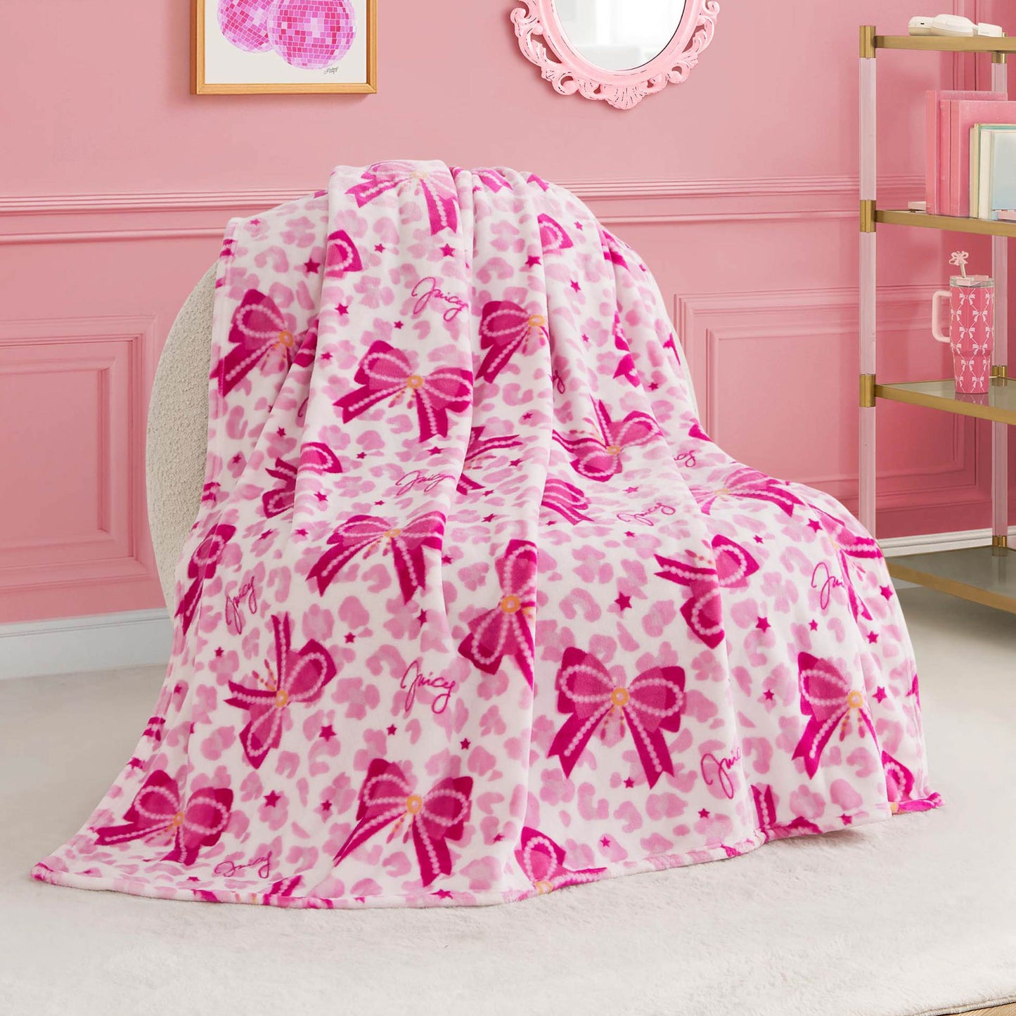 The Kids Plush Throw Blanket features pink and white leopard print with pink bow designs, draped over a round chair in a pink-themed room. This ultra-soft blanket adds cozy style and is perfect for any chic kids' space.