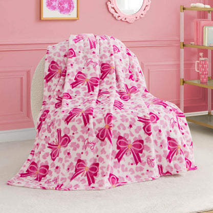 The Kids Plush Throw Blanket features pink and white leopard print with pink bow designs, draped over a round chair in a pink-themed room. This ultra-soft blanket adds cozy style and is perfect for any chic kids' space.