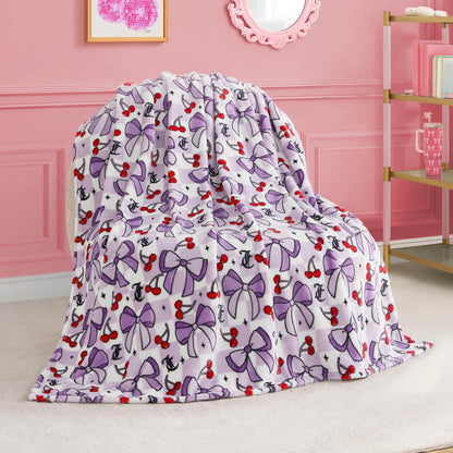 A Kids Plush Throw Blanket featuring purple bows, red cherries, and black anchors is draped over a chair in a pink room decorated with elegant accents and wall art.