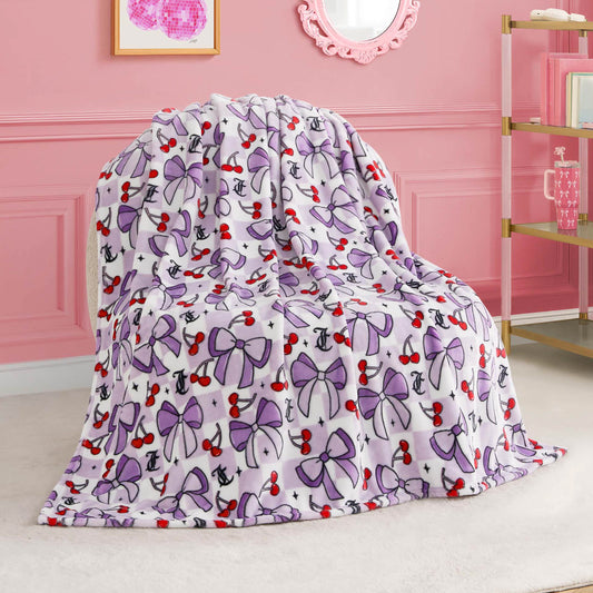 A Kids Plush Throw Blanket featuring purple bows, red cherries, and black anchors is draped over a chair in a pink room decorated with elegant accents and wall art.