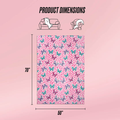 The Kids Plush Throw Blanket by Juicy Couture comes in pink with playful butterfly and heart designs. Measuring 70" x 50", it’s ultra-soft, perfect for kids, as shown draped over a sofa and person. Text displays: Product Dimensions.