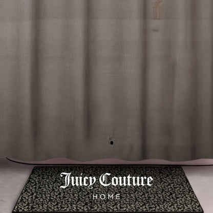 A patterned black and white doormat with Juicy Couture HOME sits in front of a sheer tan PEVA Shower Curtain Liner, which has a small hole near the bottom.