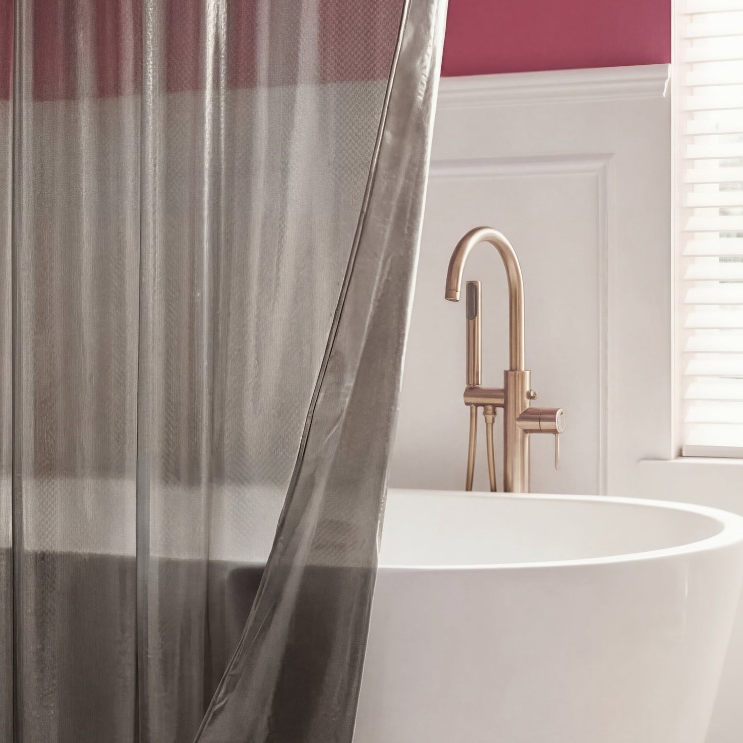 A modern bathroom with a white freestanding tub, brushed gold faucet, PEVA Shower Curtain Liner, and a pink accent wall featuring white wainscoting and window blinds.