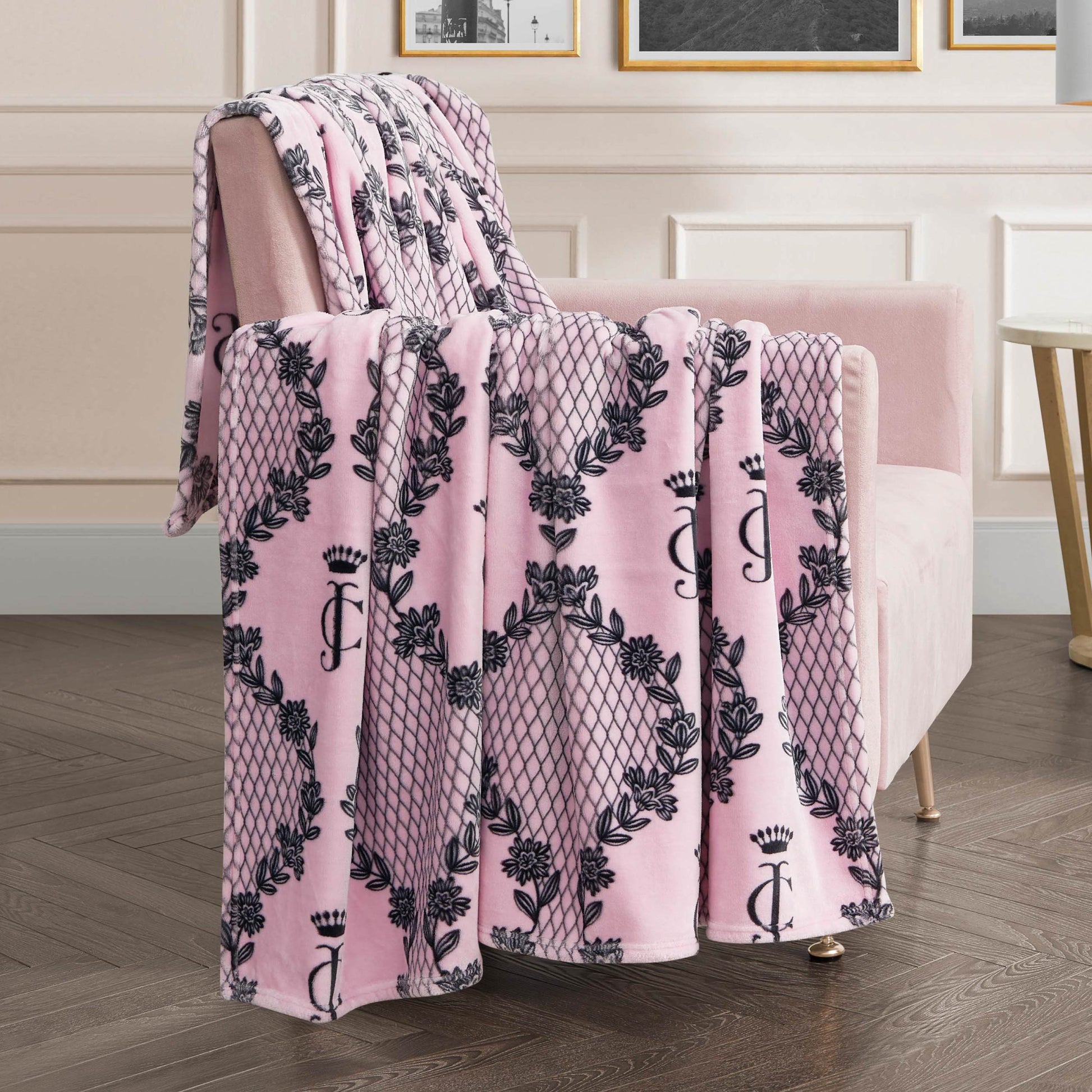 A pink velvet armchair with a Plush Oversized Throw Blanket featuring black floral and lattice designs, monogrammed with a J and crown, brings chic style to any modern living room.