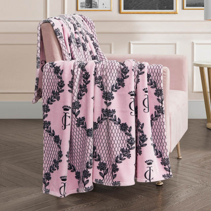 A pink velvet armchair with a Plush Oversized Throw Blanket featuring black floral and lattice designs, monogrammed with a J and crown, brings chic style to any modern living room.