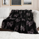 A Plush Oversized Throw Blanket with pink bow accents and "juicy" lettering is draped over a white couch in a chic living room, adding an ultra-soft touch beneath framed wall art.