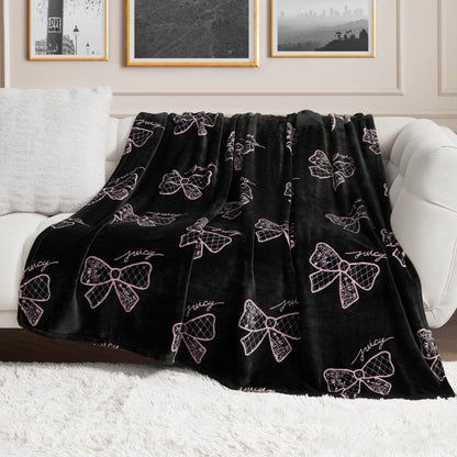 A Plush Oversized Throw Blanket with pink bow accents and "juicy" lettering is draped over a white couch in a chic living room, adding an ultra-soft touch beneath framed wall art.
