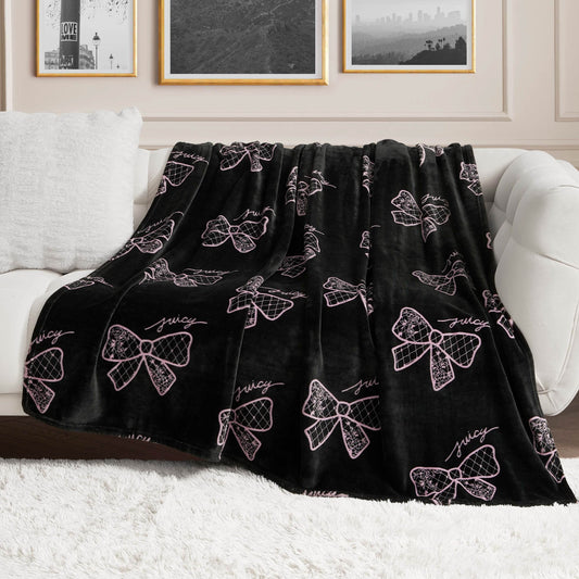 A Plush Oversized Throw Blanket with pink bow accents and "juicy" lettering is draped over a white couch in a chic living room, adding an ultra-soft touch beneath framed wall art.