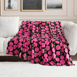 The Plush Oversized Throw Blanket, featuring vibrant pink roses and green leaves on a black background, is draped over a white couch in a bright, elegant living room decorated with framed artwork.