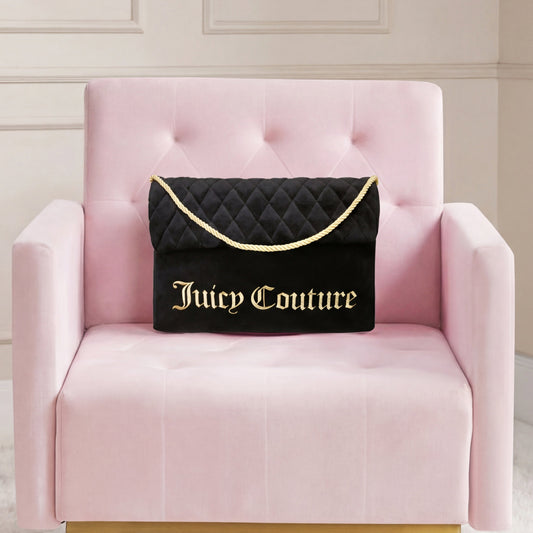 A Purse Decorative Pillow designed to look like a black quilted bag with gold chain and lettering rests on a light pink velvet chair in a cream-paneled room.