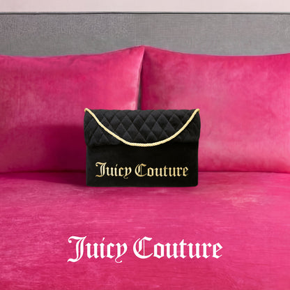 A Purse Decorative Pillow inspired by Juicy Couture, featuring black fabric with gold lettering and a gold rope handle, sits on a bright pink velvet bed accented with matching trendy pillows. The Juicy Couture logo appears in white on the bed.