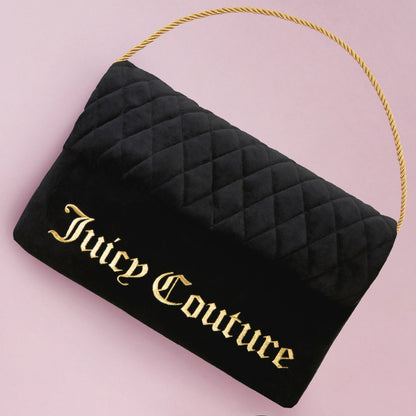 A Purse Decorative Pillow inspired by a black quilted Juicy Couture handbag with a gold rope handle and bold gold "Juicy Couture" lettering, styled on a light pink background next to a chic accent pillow for added flair.