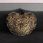 The Heart Shaped Decorative Pillow, featuring a ruffled edge and cheetah print inspired by Juicy Couture, rests on a dark gray velvet sofa with a gray backrest.