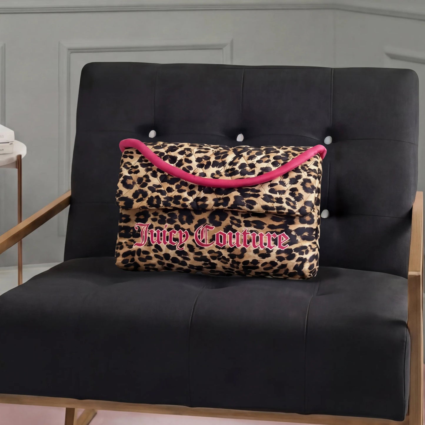 A Purse Decorative Pillow with leopard print, pink trim, and bold Juicy Couture lettering adds a trendy touch to a modern black armchair with wooden armrests in a stylish room.