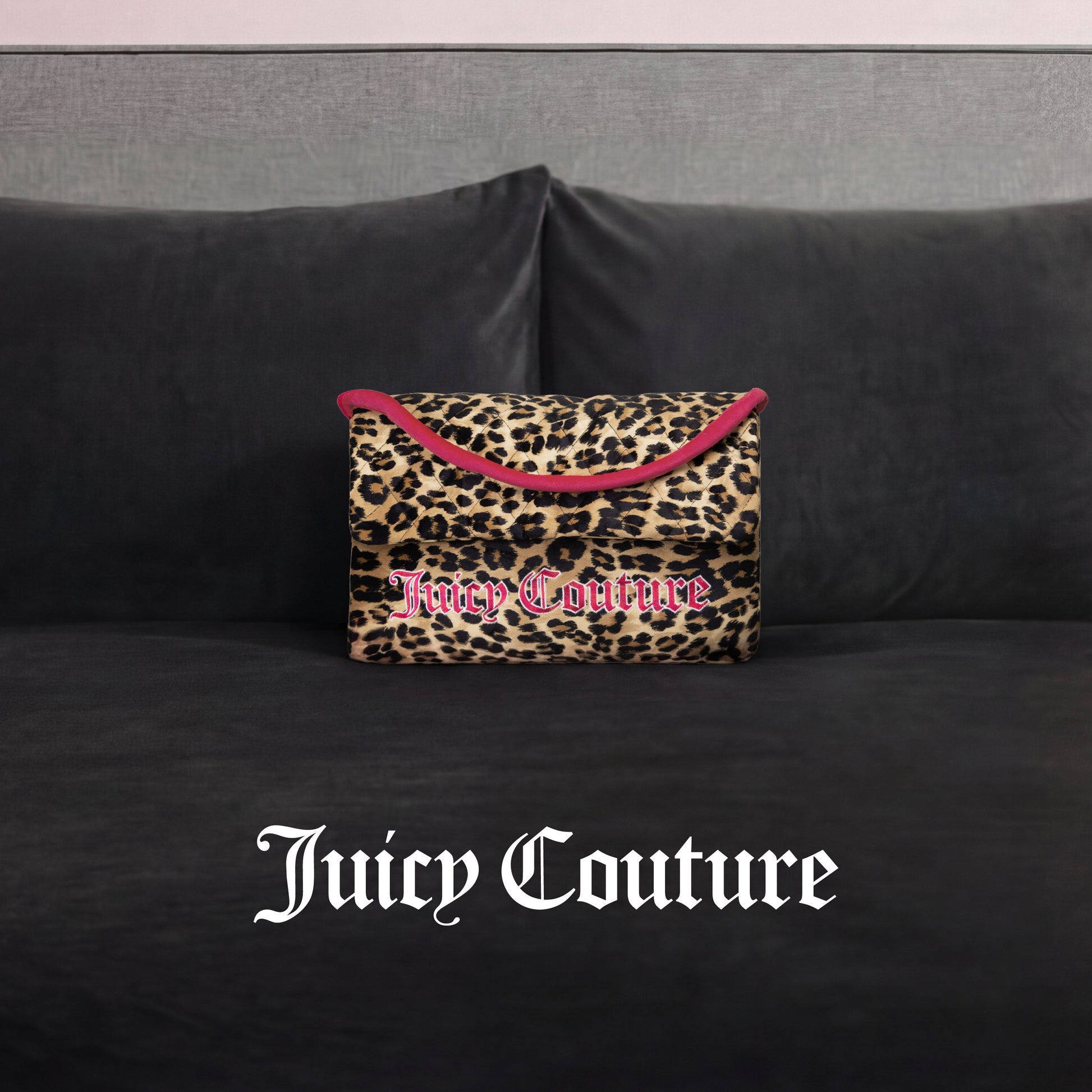 A Juicy Couture Purse Decorative Pillow with leopard print and pink trim accents a dark gray velvet couch. The white Gothic "Juicy Couture" logo appears at the image's bottom, adding trendy flair.