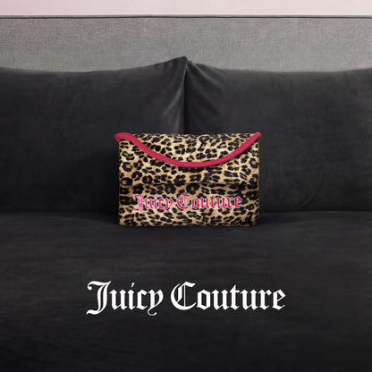 A Juicy Couture Purse Decorative Pillow with leopard print and pink trim accents a dark gray velvet couch. The white Gothic "Juicy Couture" logo appears at the image's bottom, adding trendy flair.