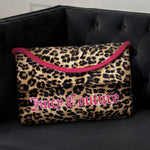 A Purse Decorative Pillow with leopard print, bold pink trim, and large Juicy Couture lettering sits on a tufted black velvet sofa, adding a trendy accent to any chic room.